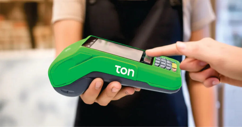 Um empreendedor utiliza uma maquininha de cartão verde da marca Ton enquanto um cliente realiza o pagamento por aproximação (NFC). A imagem ilustra de forma moderna e profissional como usar a maquininha Ton no dia a dia do comércio.