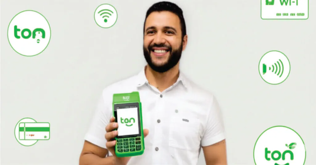 Um pequeno empreendedor sorridente segura uma maquininha de cartão verde da marca Ton, com ícones de Wi-Fi, Pix e cartão de crédito flutuando ao redor, em um fundo branco e moderno.